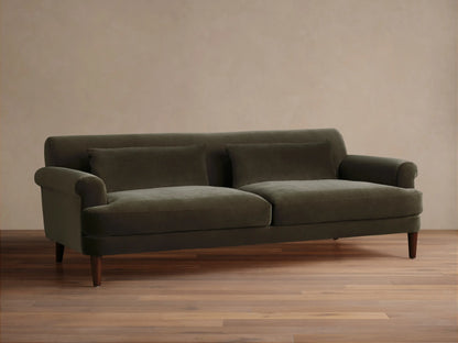 Thorne Sofa in dark olive green velvet, front view, with two seat cushions, two back pillows, and dark wood legs, on a wood floor.