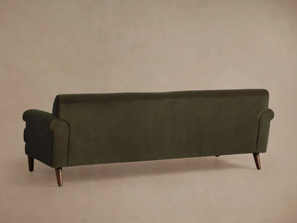 Angled view of the Thorne Sofa. Dark olive green velvet upholstery, featuring a rounded armrest, seat cushions, and dark wooden leg.