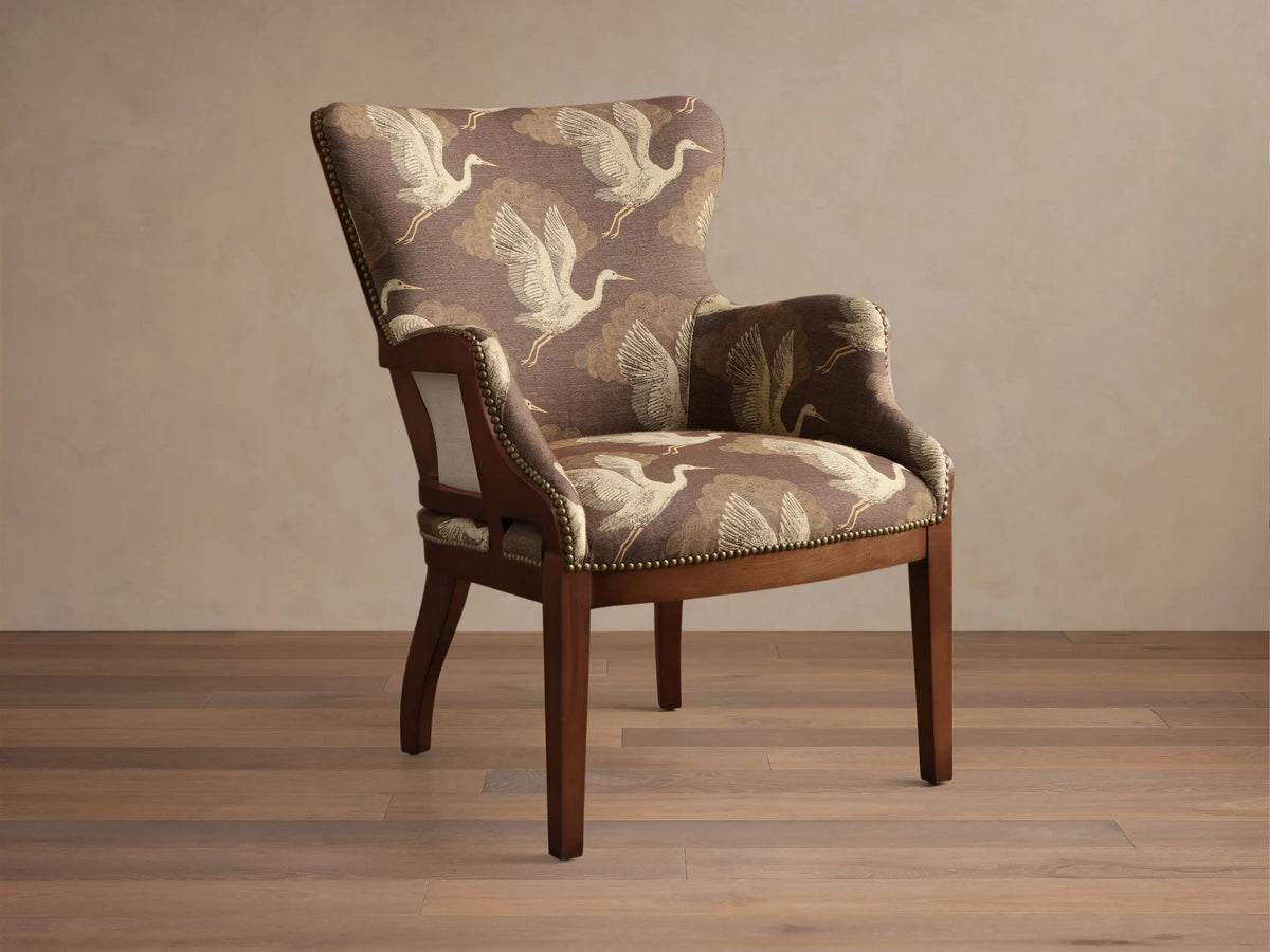 Angled view of the brown Tilly Chair with off-white crane pattern upholstery, dark wood frame, and brass nailhead detailing.