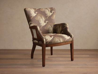 Angled view of the brown Tilly Chair with off-white crane pattern upholstery, dark wood frame, and brass nailhead detailing.