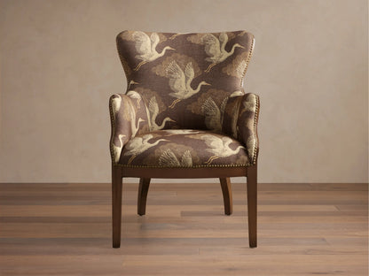 Angled view of the brown Tilly Chair with off-white crane pattern upholstery, dark wood frame, and brass nailhead detailing.