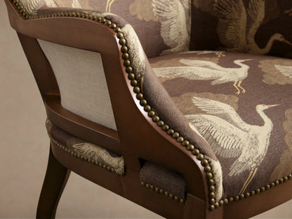 Front view of the brown Tilly Chair with beige crane and cloud pattern upholstery, dark wooden legs, and brass nailhead trim.