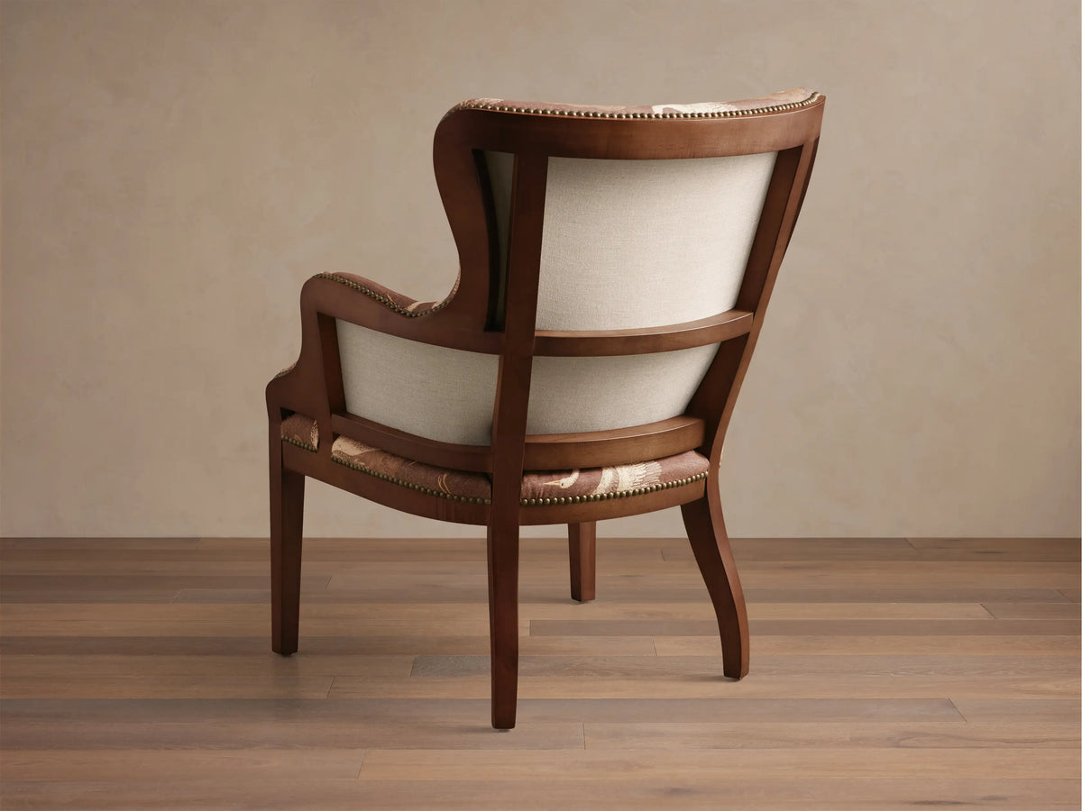 Close-up of a Tilly Chair arm, showing dark brown wood, brass nailhead trim, and brown fabric with a light crane pattern.