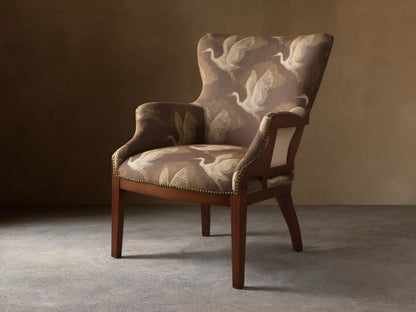 Angled view of the brown Tilly Chair with off-white crane pattern upholstery, dark wood frame, and brass nailhead detailing.