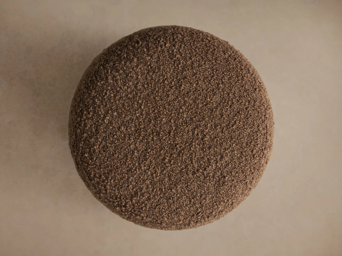 Steffi Ottoman, a round, tapered ottoman in textured brown boucle fabric, resting on three short, dark chestnut wooden legs.