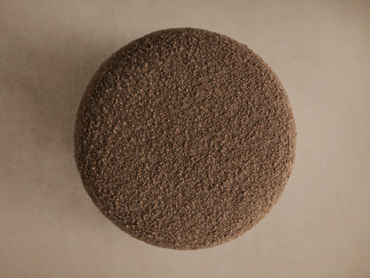 Steffi Ottoman, a round, tapered ottoman in textured brown boucle fabric, resting on three short, dark chestnut wooden legs.