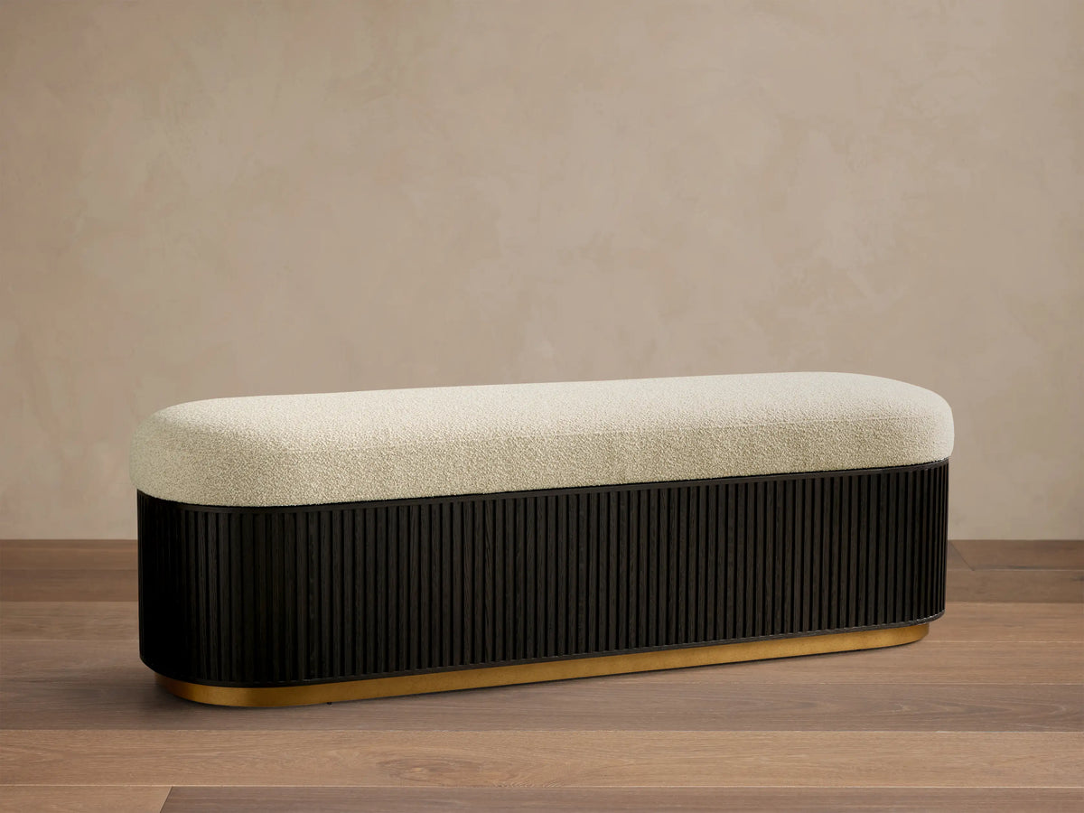 Front view of the Finnley Storage Bench™ with a cream upholstered top, an ebony fluted wooden base, and a brass trim.