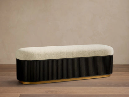 Front view of the Finnley Storage Bench™ with a cream upholstered top, an ebony fluted wooden base, and a brass trim.
