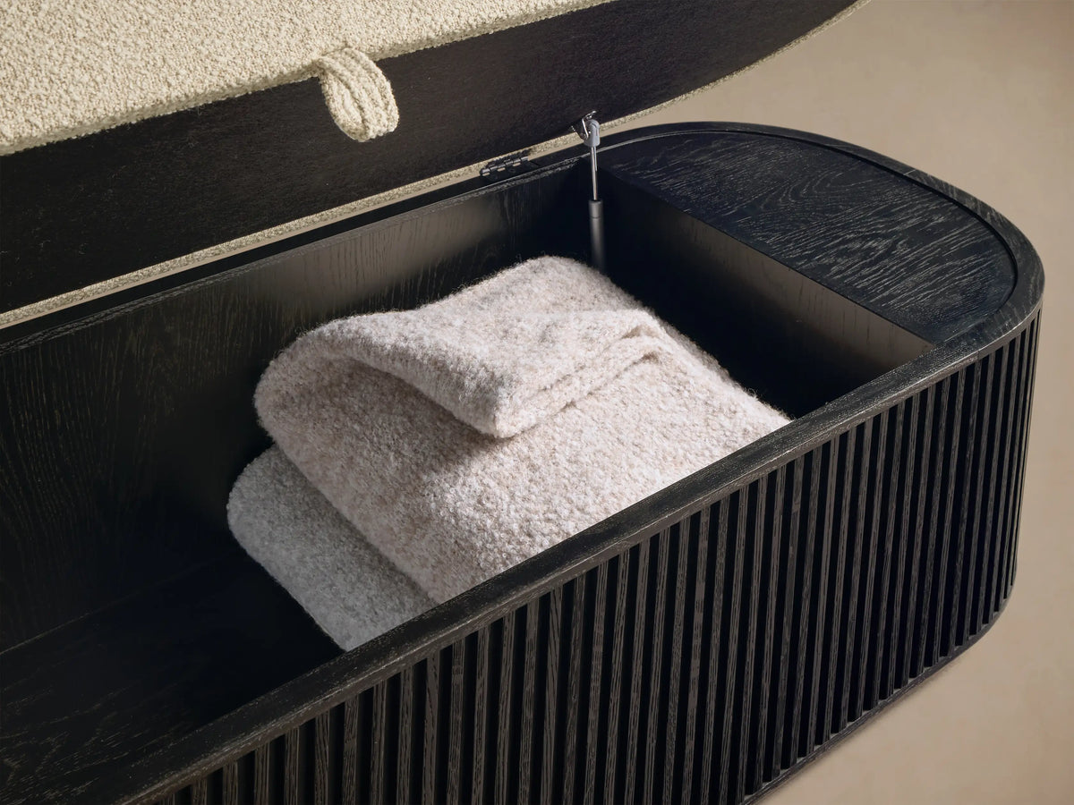 Front view of the Finnley Storage Bench with a light beige upholstered top, dark brown ribbed wood body, and golden base.