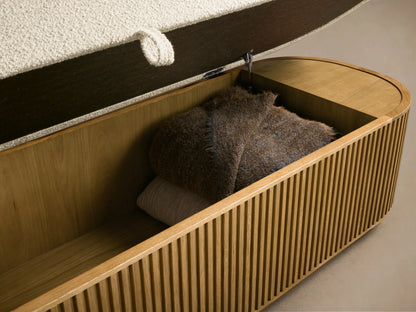Front view of the oval Finnley Storage Bench with a cream textured fabric cushion and a honey oak wood fluted base.