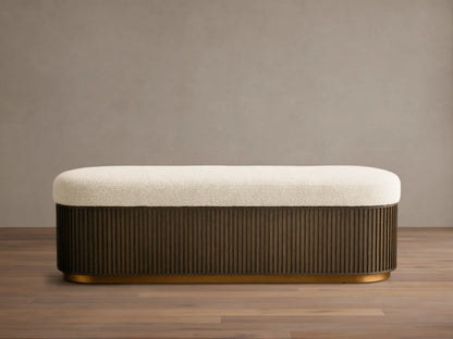 Front view of the Finnley Storage Bench, with a cream textured cushion, dark brown fluted wood base, and gold trim.
