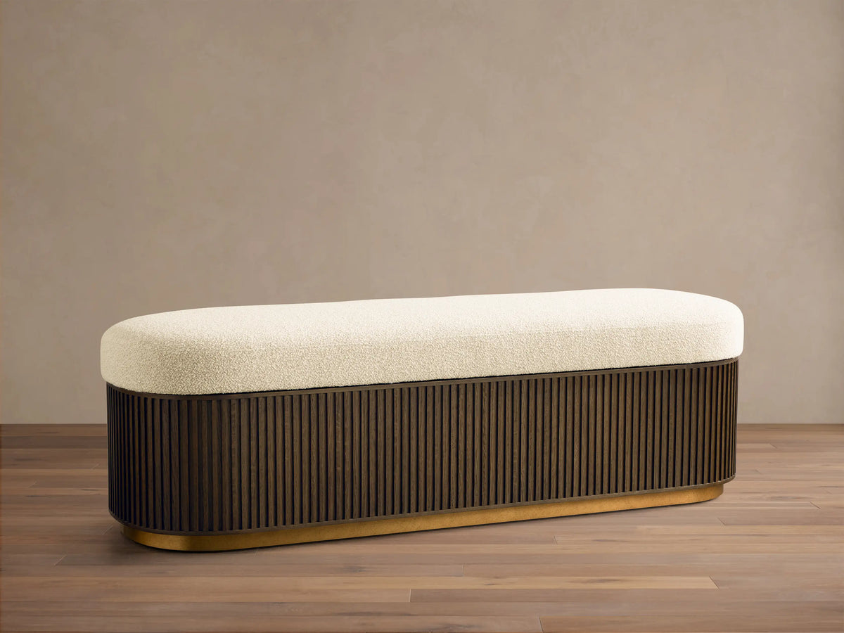 Front view of the Finnley Storage Bench with an oval cream cushion, dark slatted wood base, and a golden bottom trim.