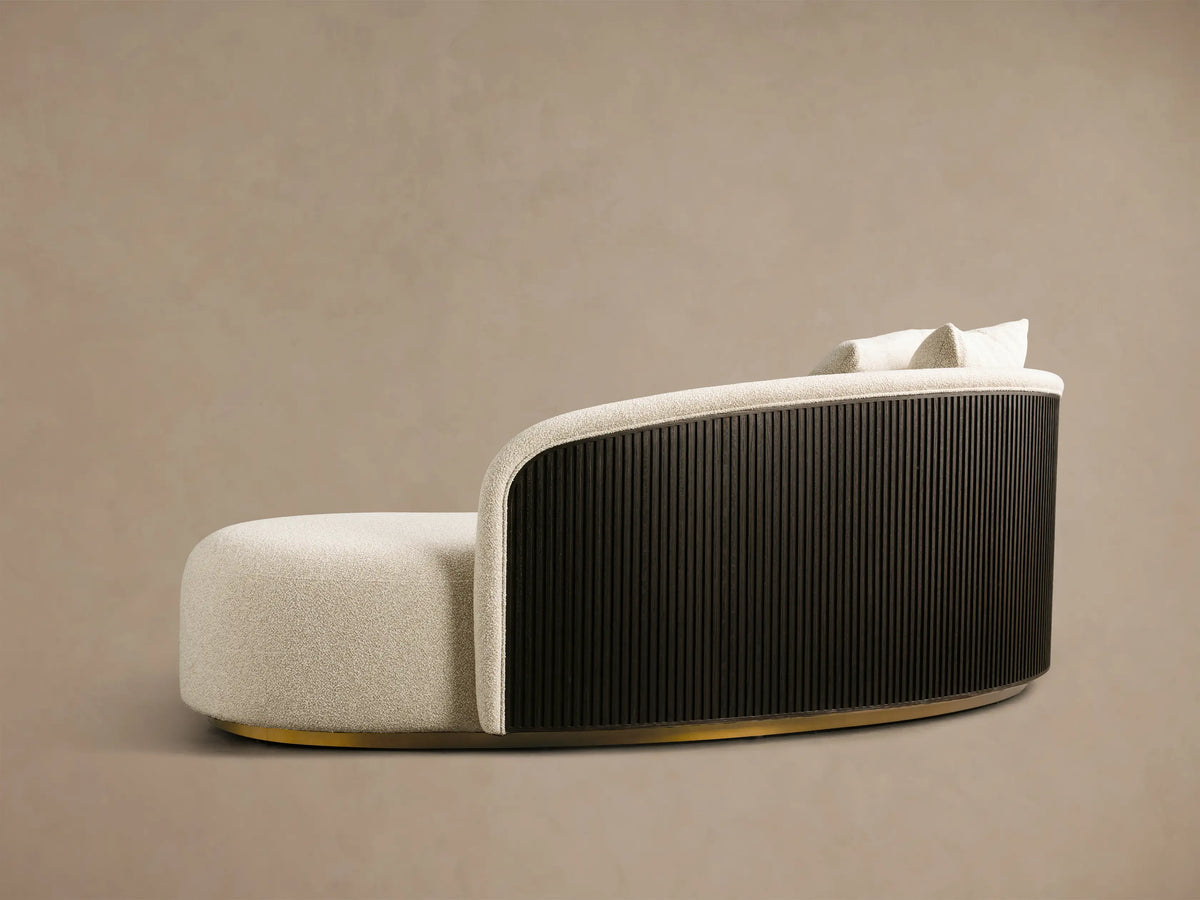 Side profile of Finnley Daybed with light textured upholstery, black slatted back, and golden base. Two matching pillows.