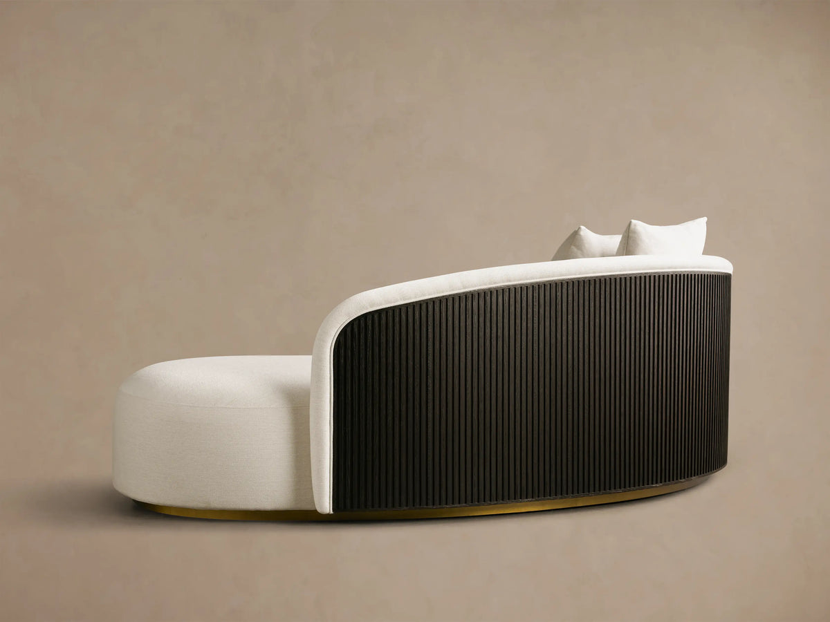 Side profile of the Finnley Daybed with cream upholstery, curved black slatted back, and gold base. Two cream toss pillows are on top.
