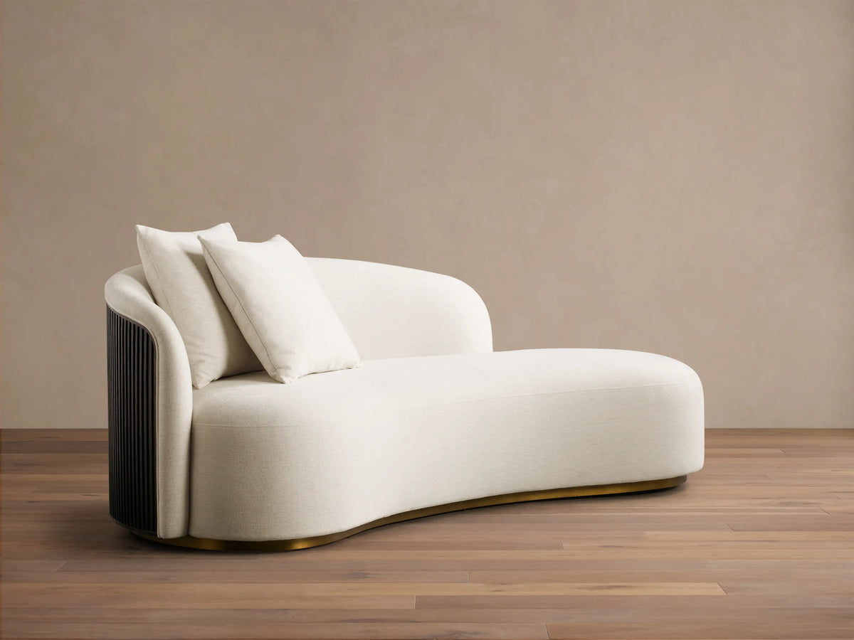 Front view of a cream Finnley Daybed with a curved shape, dark ribbed wood panel, two matching pillows, and a brass base.
