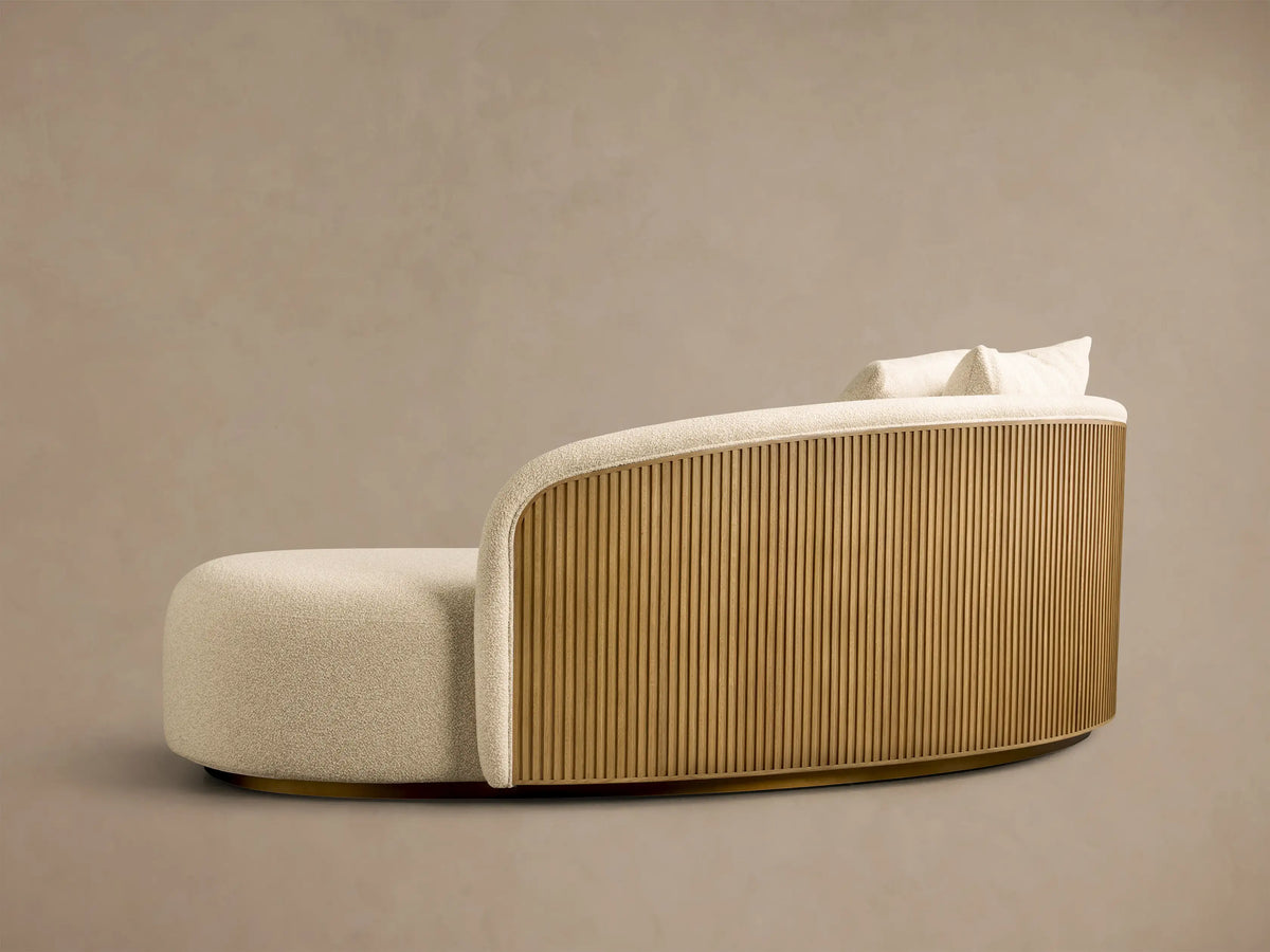 Front view of a cream Finnley Daybed, featuring a curved shape, slatted honey wood side, golden base, and two toss pillows.
