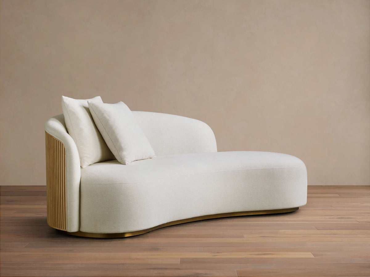 Front view of an off-white Finnley Daybed with a curved back and seat, two matching throw pillows, and a brass-toned base.