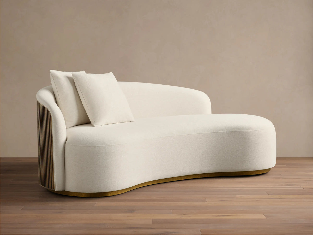 Front view of the Off-white Finnley Daybed, an asymmetrical daybed with two matching pillows and a curved gold-toned base.