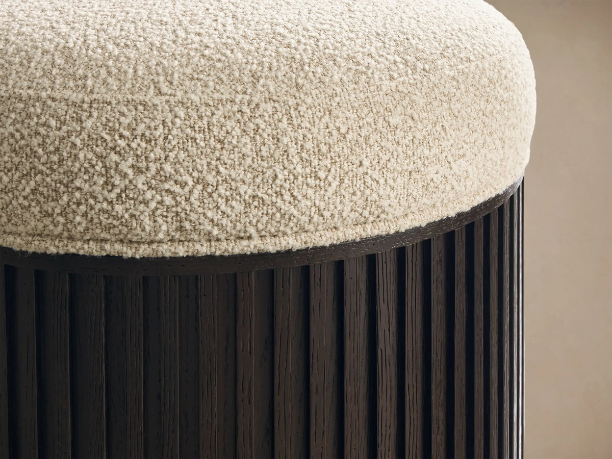 Close-up of the Finnley Ottoman, featuring a cream textured bouclv© top and a dark brown fluted wood base.