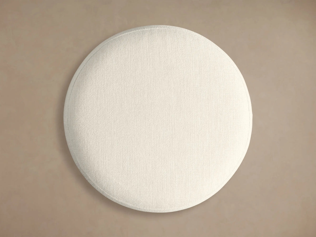 Front view of the Finnley Ottoman featuring a cream upholstered cushion, an Ebony vertical ribbed wood base, and a brass-colored circular trim.