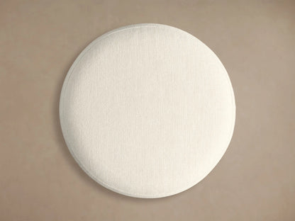 Front view of the Finnley Ottoman featuring a cream upholstered cushion, an Ebony vertical ribbed wood base, and a brass-colored circular trim.