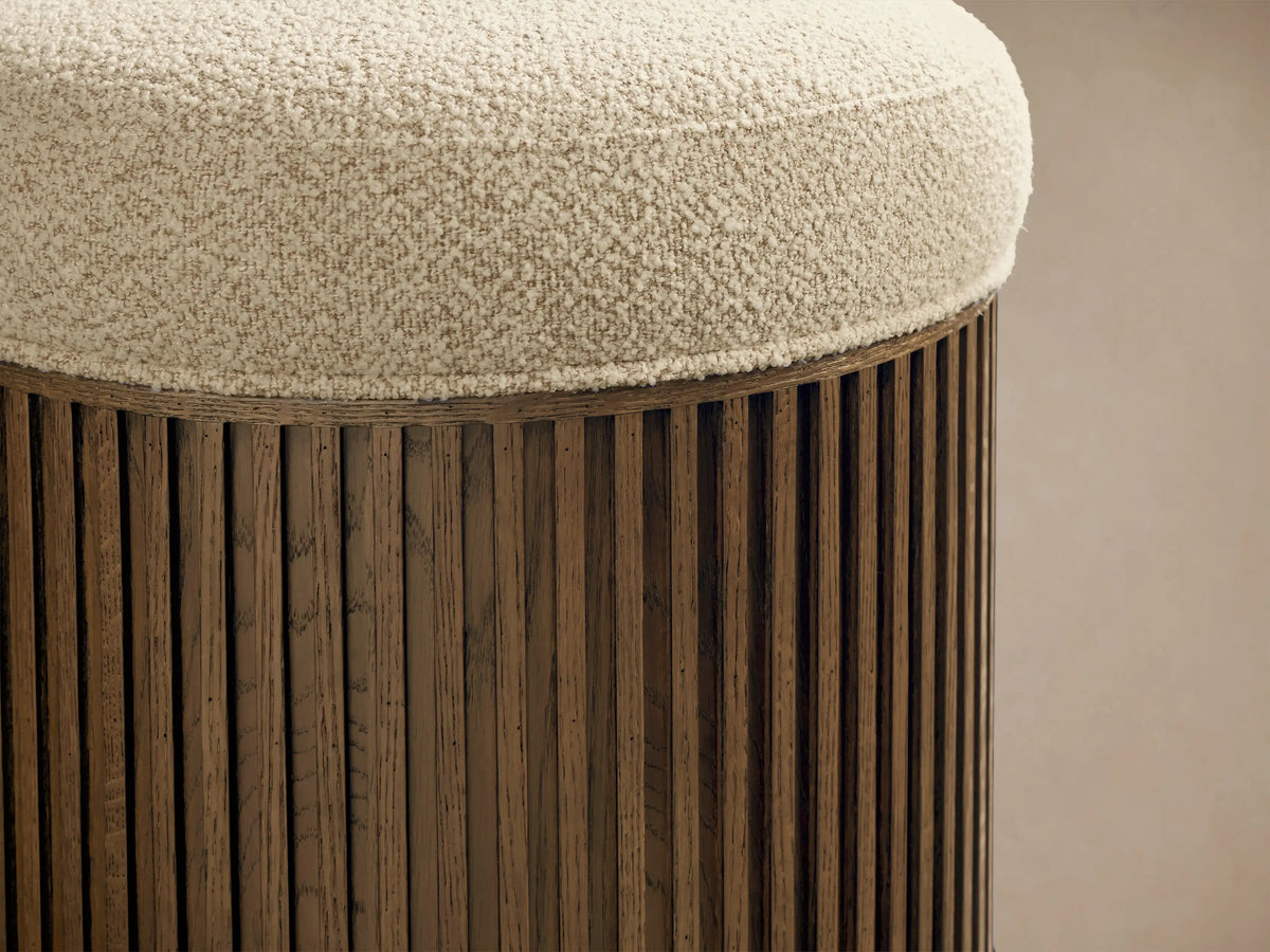 Close-up of the Finnley Ottoman. Cream bouclv© upholstered top, with a dark brown slatted wood cylindrical base.