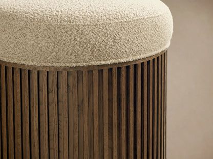 Close-up of the Finnley Ottoman. Cream bouclv© upholstered top, with a dark brown slatted wood cylindrical base.