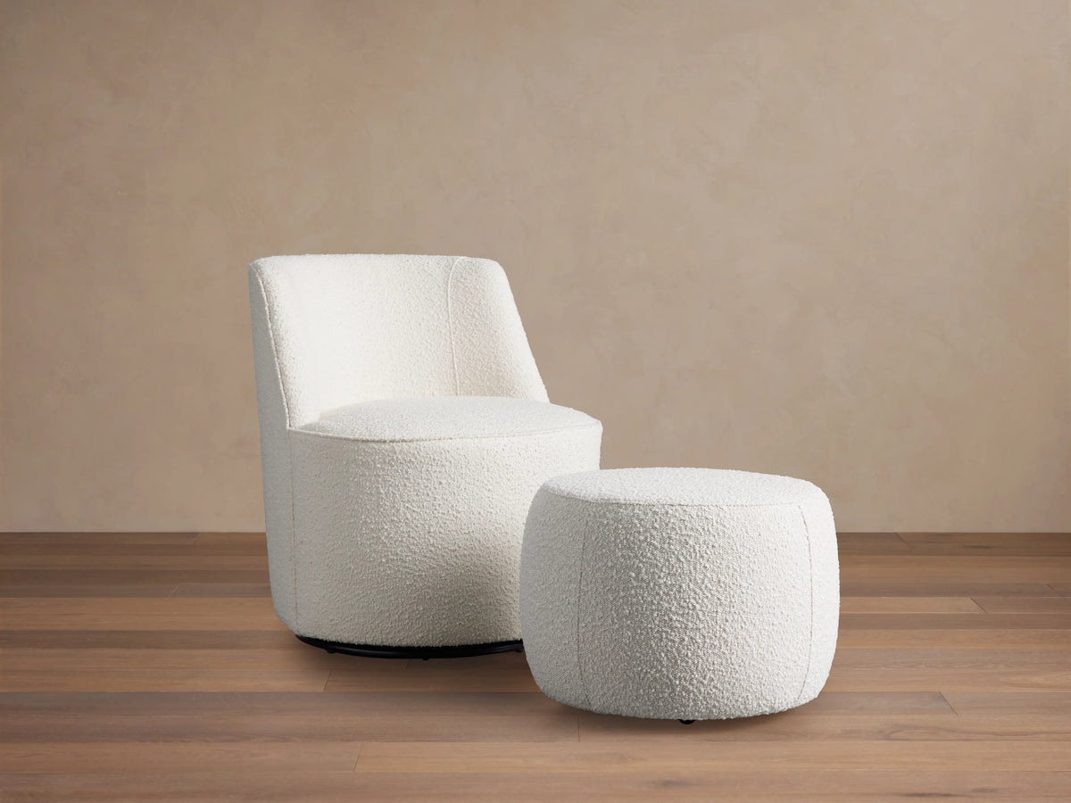 A plush, off-white Ryles Ottoman with a textured fabric surface, placed in front of a matching rounded chair on a soft brown background.