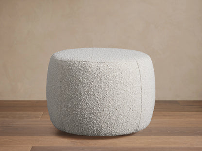 Ryles Ottoman in textured white fabric, beside a matching chair on a wooden floor, set against a beige wall background.