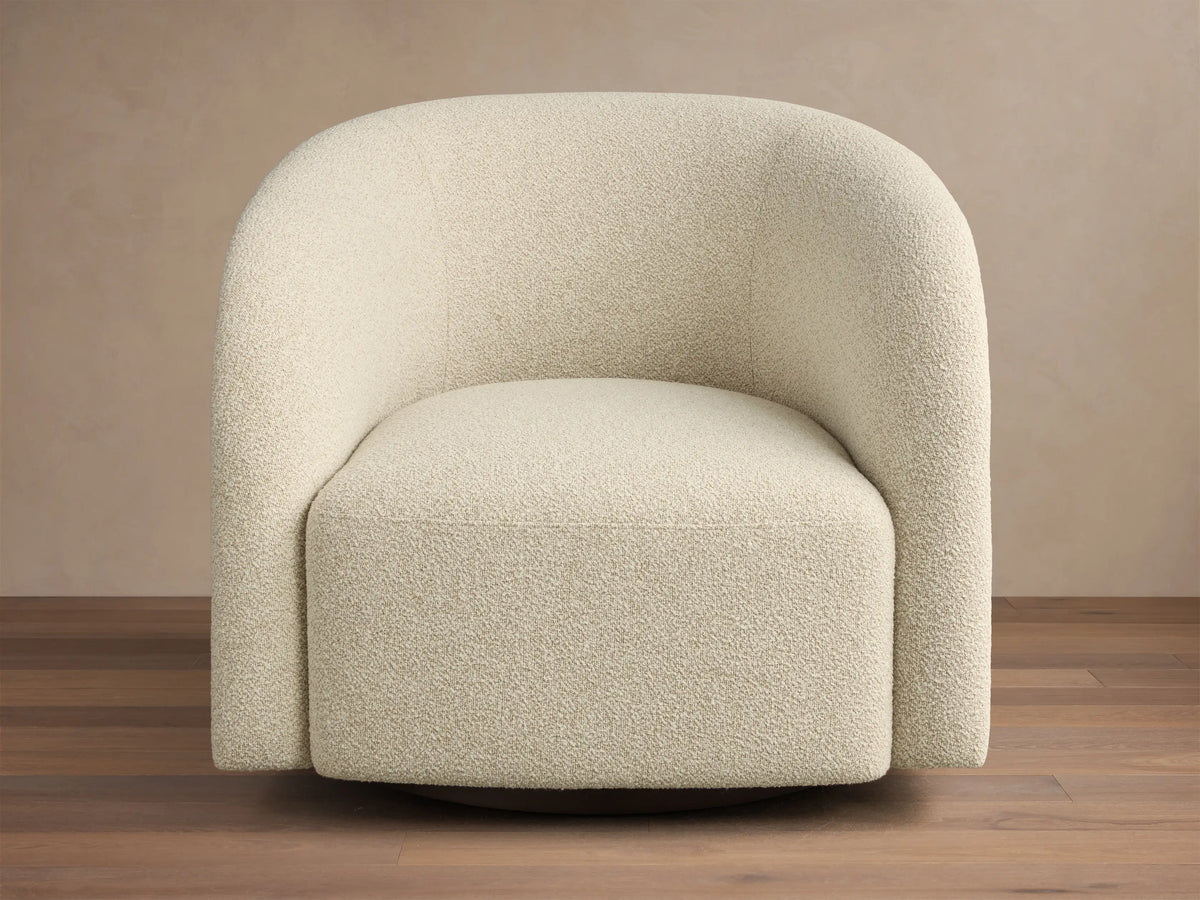 Front-side view of a cream upholstered swivel armchair with a curved back and a medium brown wood side panel.