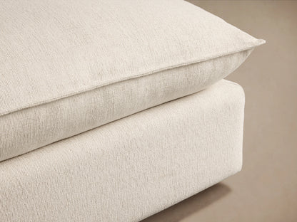 Owen Ottoman in a light beige fabric, featuring a plush, cushioned top and caster wheels on a wooden floor against a neutral wall.