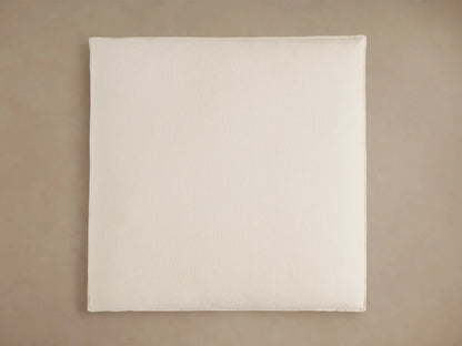 Owen Ottoman in close-up, showcasing beige textured fabric with visible stitching, featuring a plush cushion on top, and blurred neutral background.