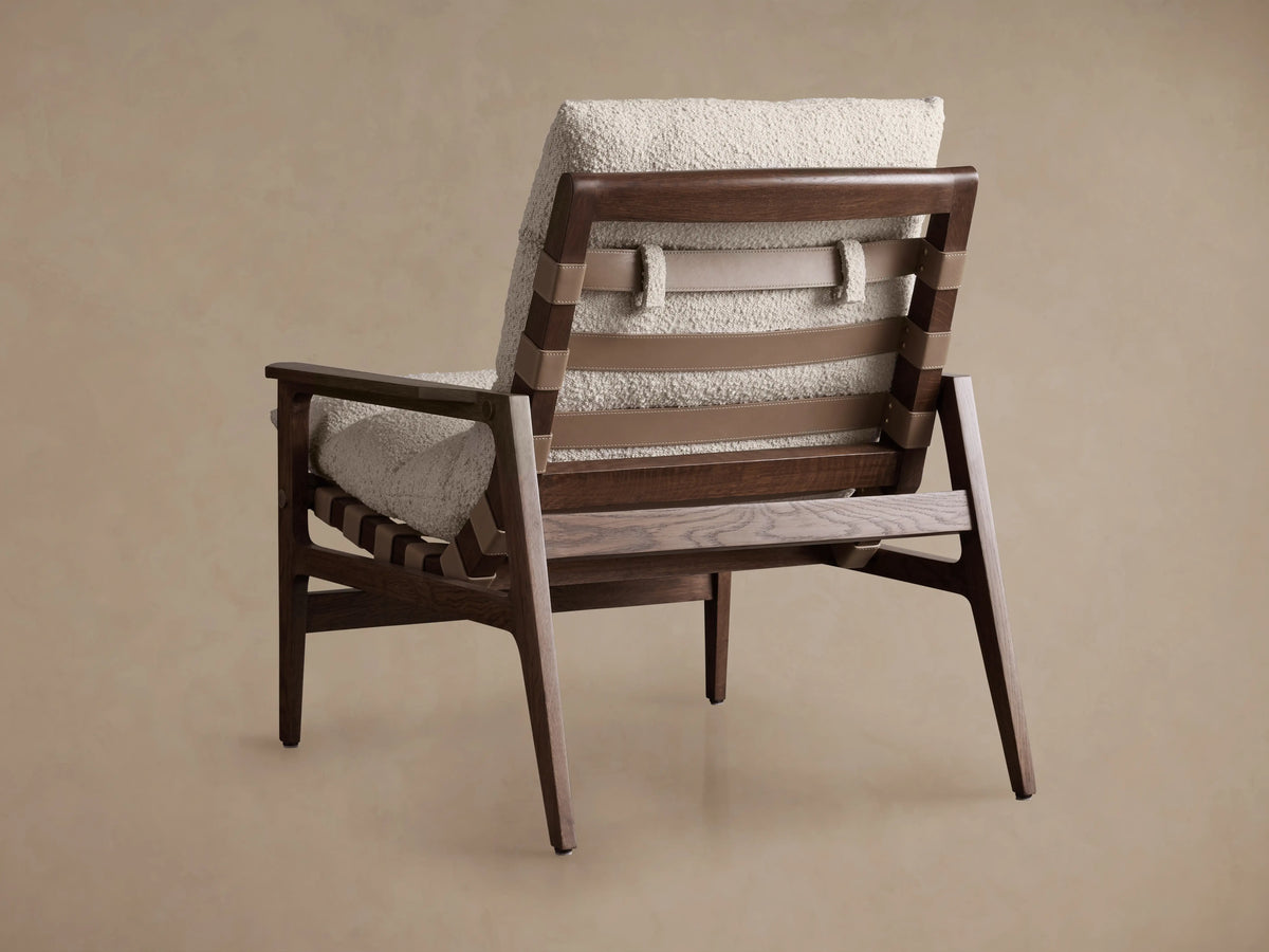 Rourke Chair with a slingback design, featuring solid wooden frame, hand-stitched leather straps, and sand-toned bouclé cushions.