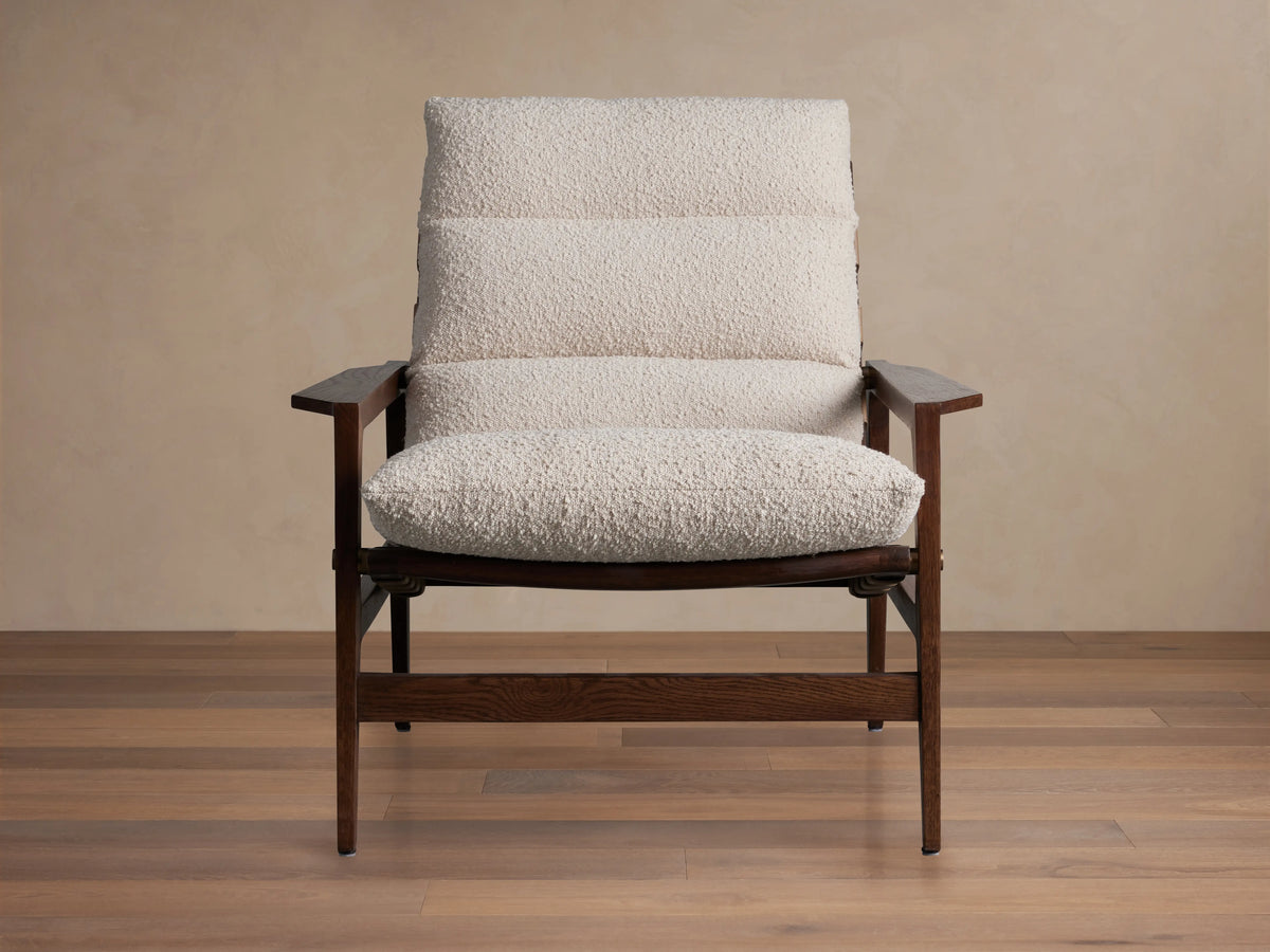 Rourke Chair in front view with wood frame, hand-stitched leather straps, sand-toned bouclé fabric cushions, and brass accents.