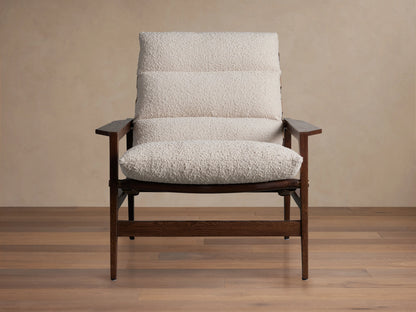 Rourke Chair in front view with wood frame, hand-stitched leather straps, sand-toned bouclé fabric cushions, and brass accents.