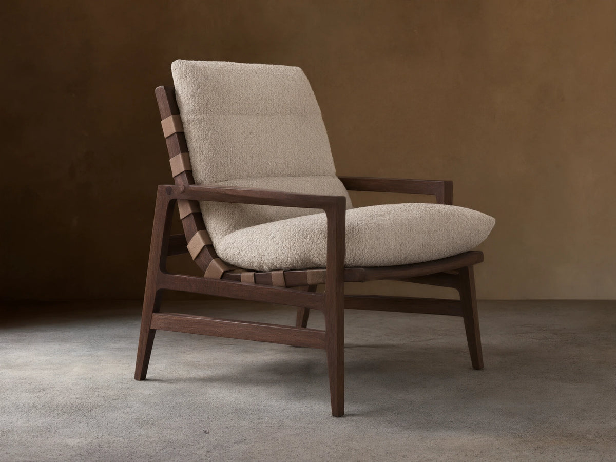 Rourke Chair with solid hardwood frame, neutral sand bouclé cushions, leather straps, and brass accents on a wood floor.