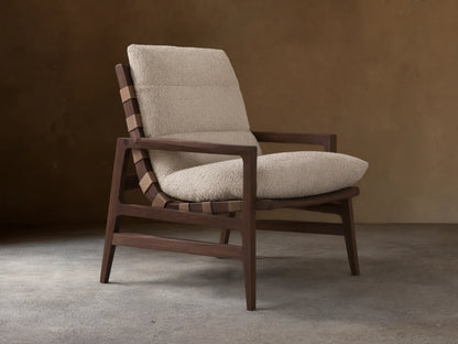 Rourke Chair with solid hardwood frame, neutral sand bouclé cushions, leather straps, and brass accents on a wood floor.
