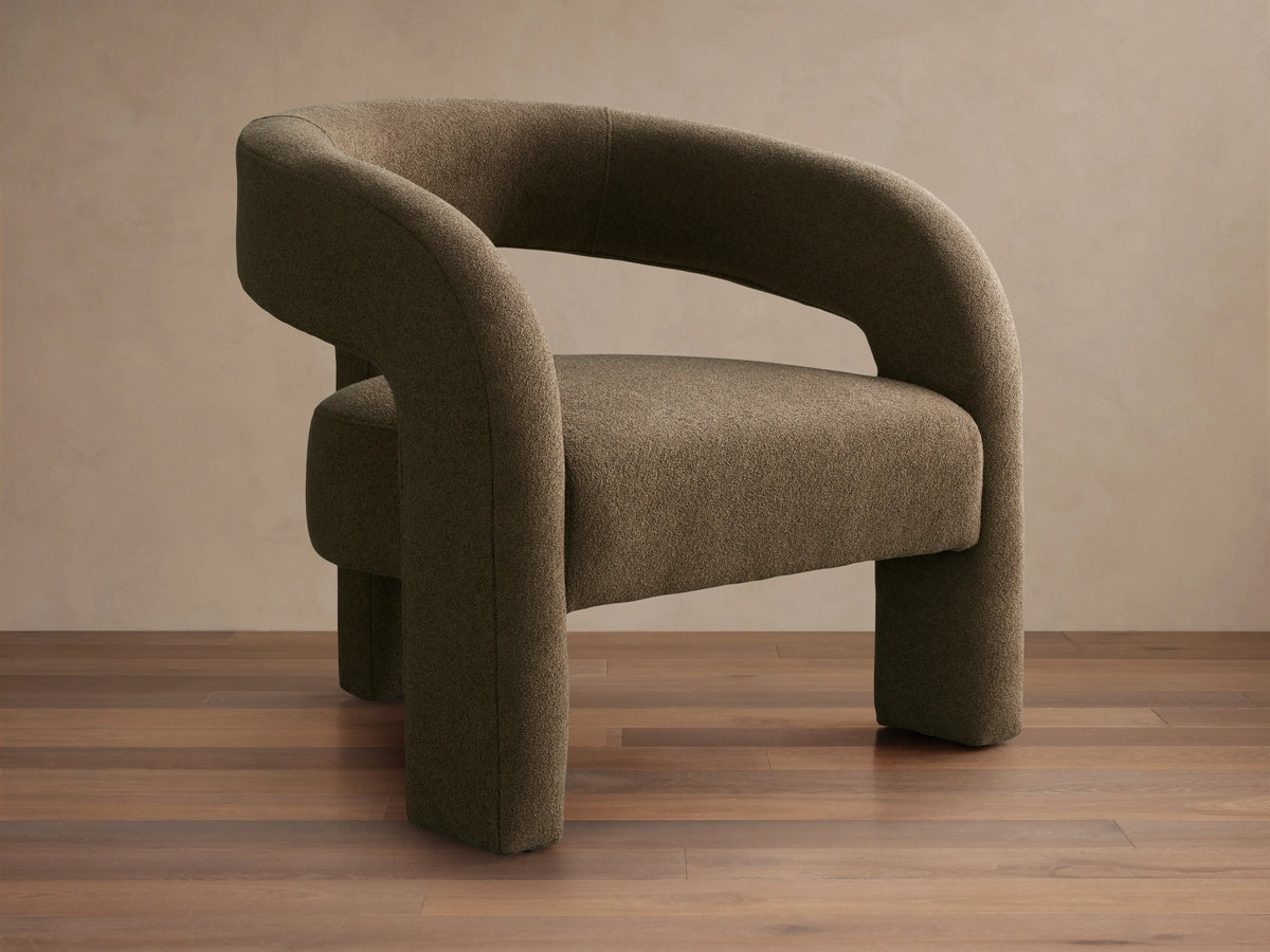 Mara Cutout Chair in taupe fabric, showcasing a rounded backrest and cutout design. Positioned on a wooden floor.