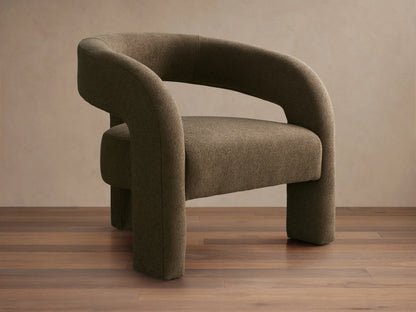 Mara Cutout Chair in taupe fabric, showcasing a rounded backrest and cutout design. Positioned on a wooden floor.
