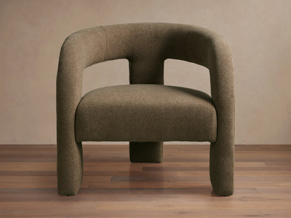 Mara Cutout Chair in taupe fabric, showcasing a rounded backrest and cutout design. Positioned on a wooden floor.