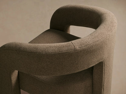 Mara Cutout Chair in taupe fabric, featuring a unique cutout design with curved arms and back, on a wooden floor background.