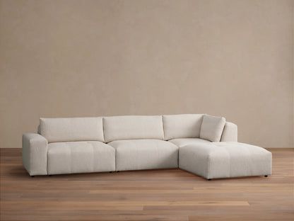 Keegan Four Piece Sectional with Ottoman in light beige textured fabric, L-shaped, on a brown wood floor.