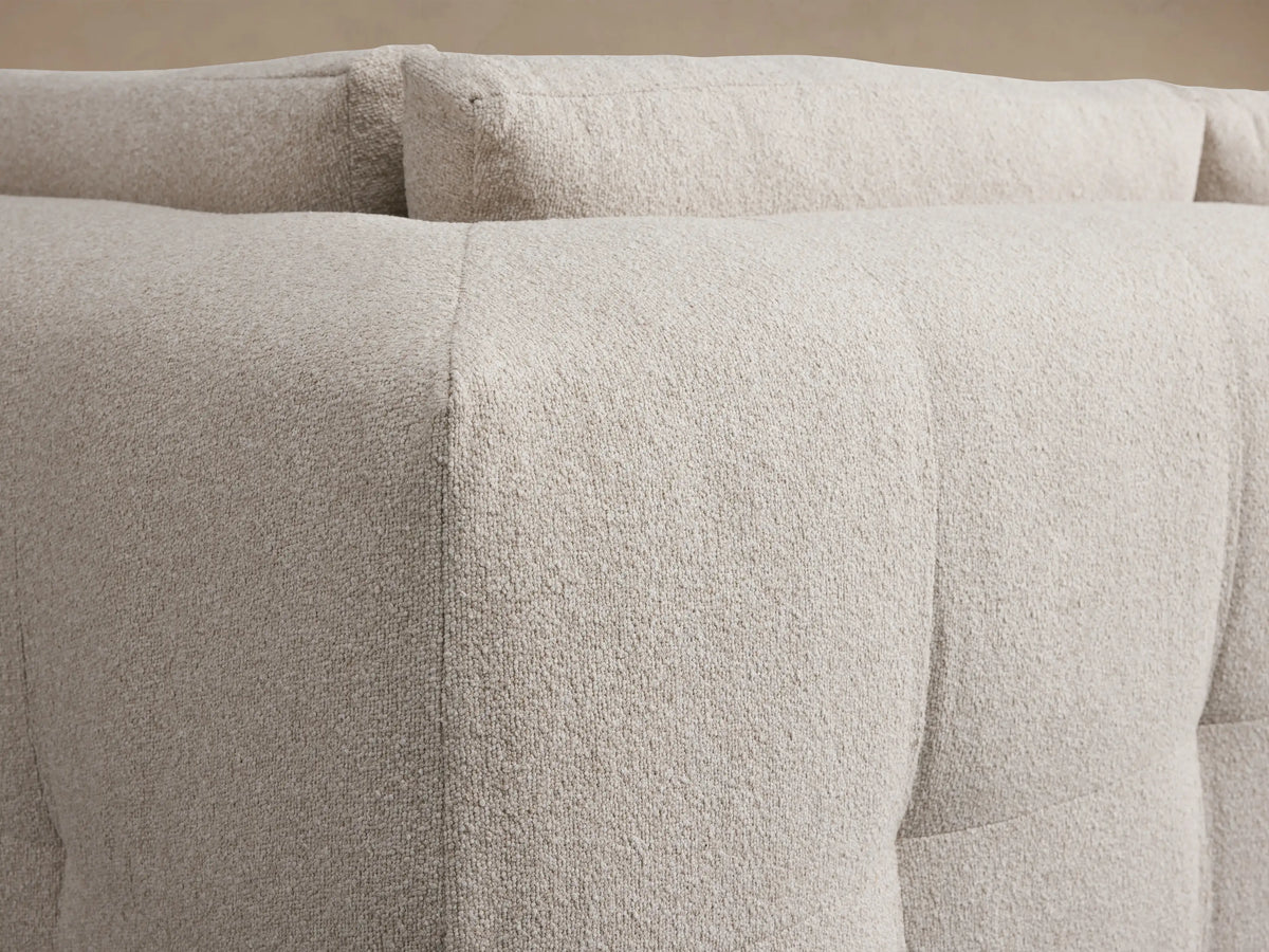 Light beige textured Keegan Four Piece Sectional with Ottoman, L-shaped, on wooden floor against a plain beige wall.