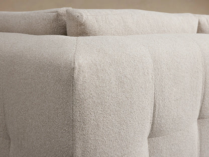 Light beige textured Keegan Four Piece Sectional with Ottoman, L-shaped, on wooden floor against a plain beige wall.