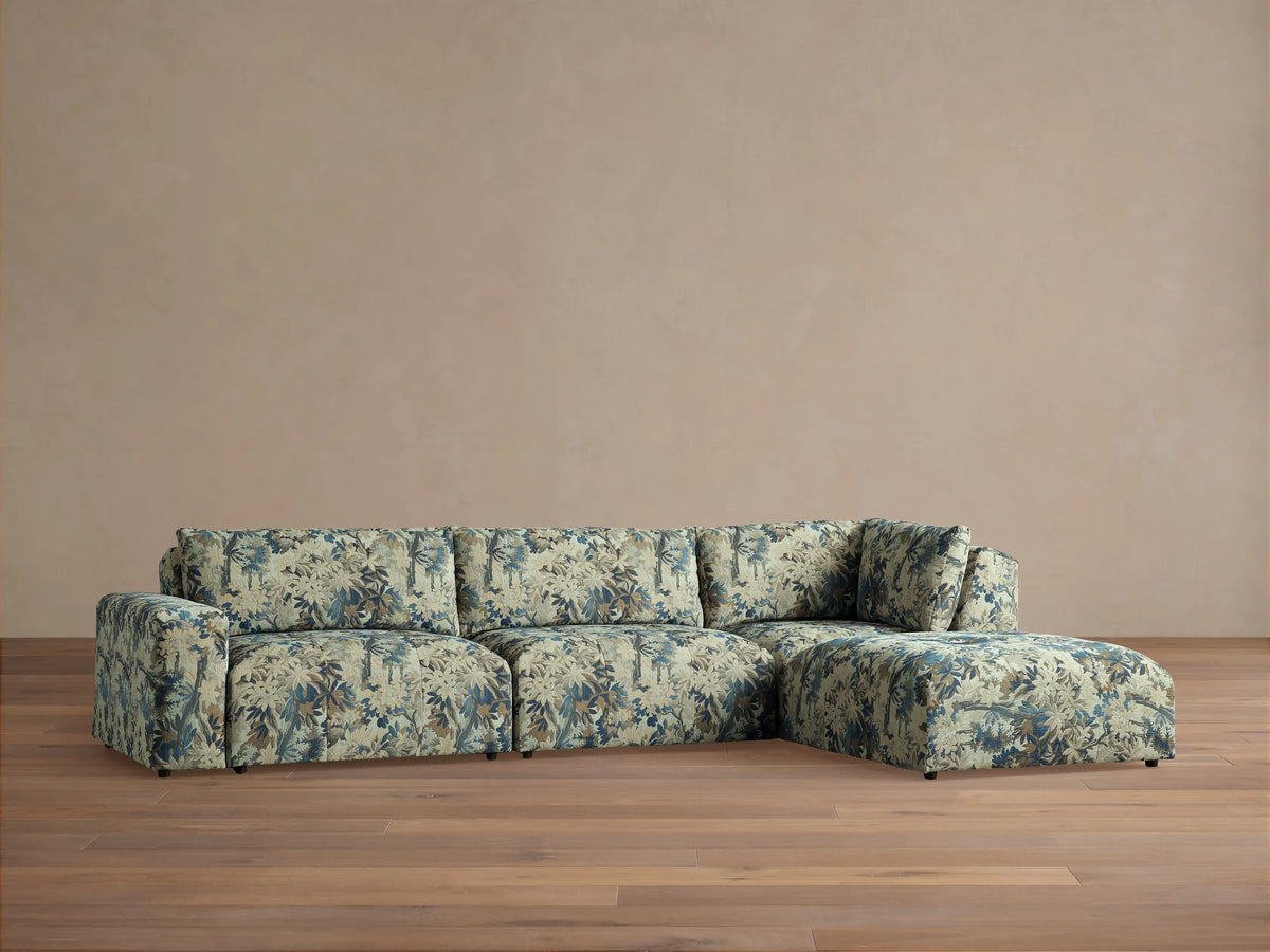 Keegan Four Piece Sectional with Ottoman, blue and beige botanical pattern, L-shaped, on a wooden floor against a beige wall.