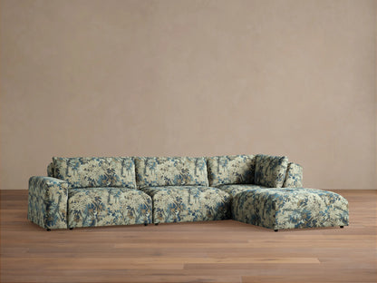 Keegan Four Piece Sectional with Ottoman, blue and beige botanical pattern, L-shaped, on a wooden floor against a beige wall.