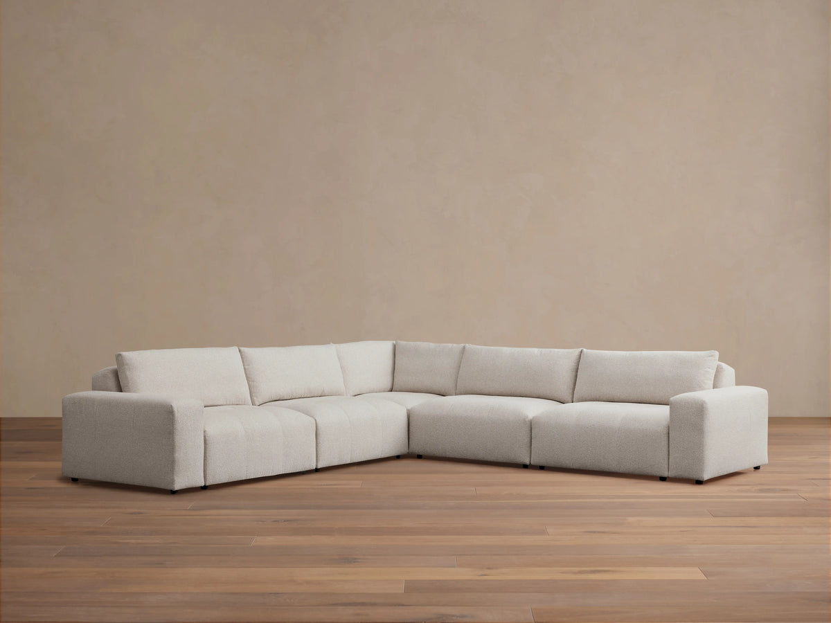Keegan Five-Piece Corner Sectional in light gray fabric, featuring a modern design with plush seat and back cushions, set on a wooden floor.