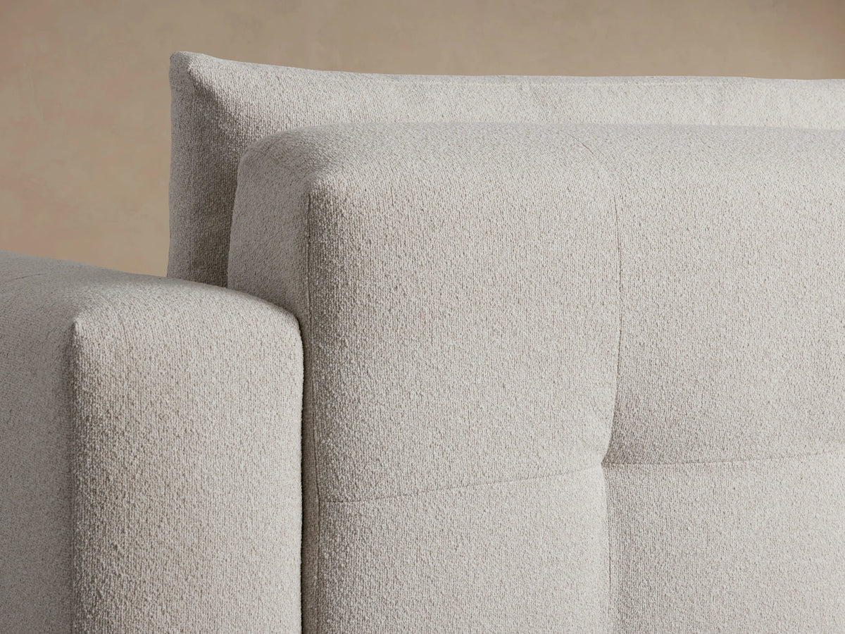 Keegan Five-Piece Corner Sectional in beige fabric, L-shaped design on wooden floor, against a beige wall. Plush cushions, low-profile.