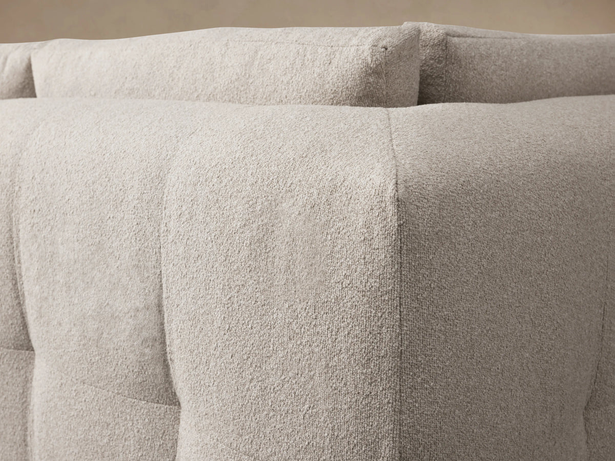 Keegan Five-Piece Sectional in light beige fabric, arranged in an L-shape. It has plush cushions, flat armrests, and is set on a wooden floor.