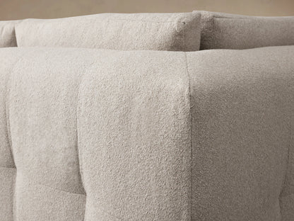 Keegan Five-Piece Sectional in light beige fabric, arranged in an L-shape. It has plush cushions, flat armrests, and is set on a wooden floor.